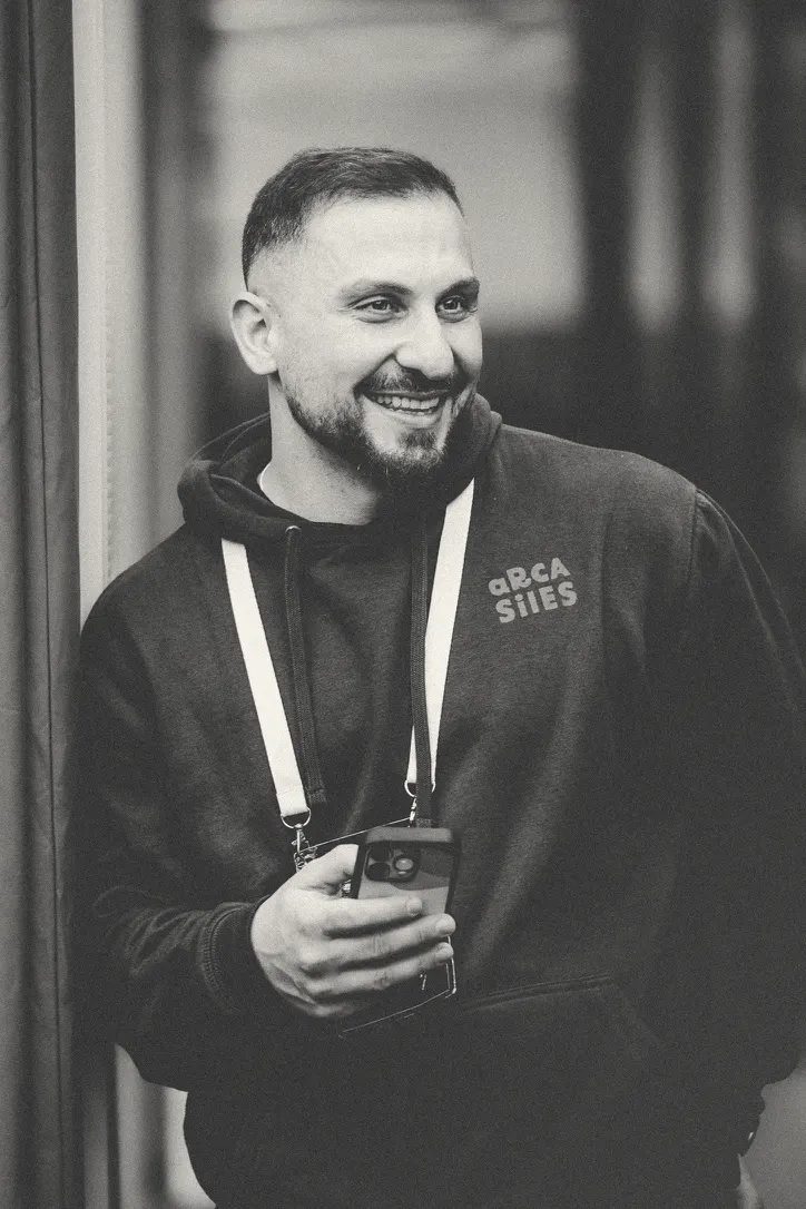 Dachi leaning on a doorframe in an Arcasiles hoodie, laughing at something off-camera, phone in hand.