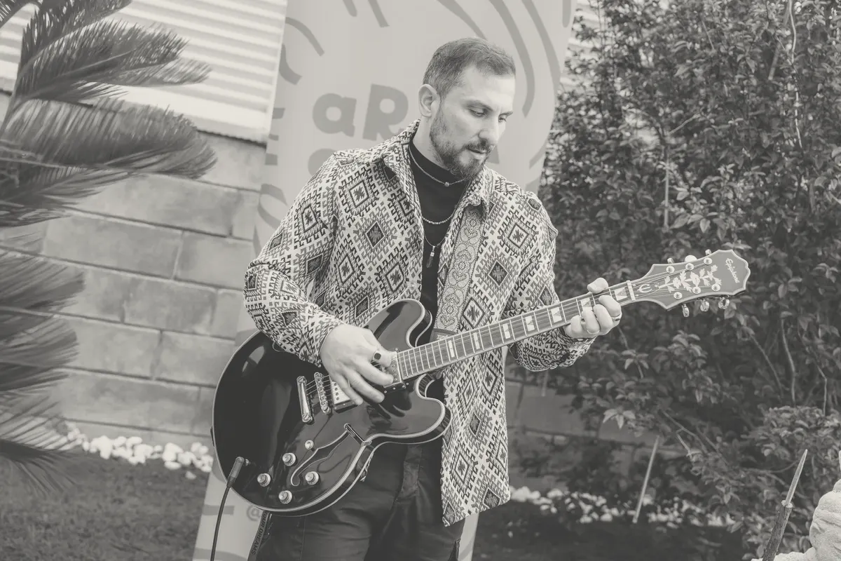 Playing a hollow-body electric guitar outdoors in front of an Arcasiles banner.