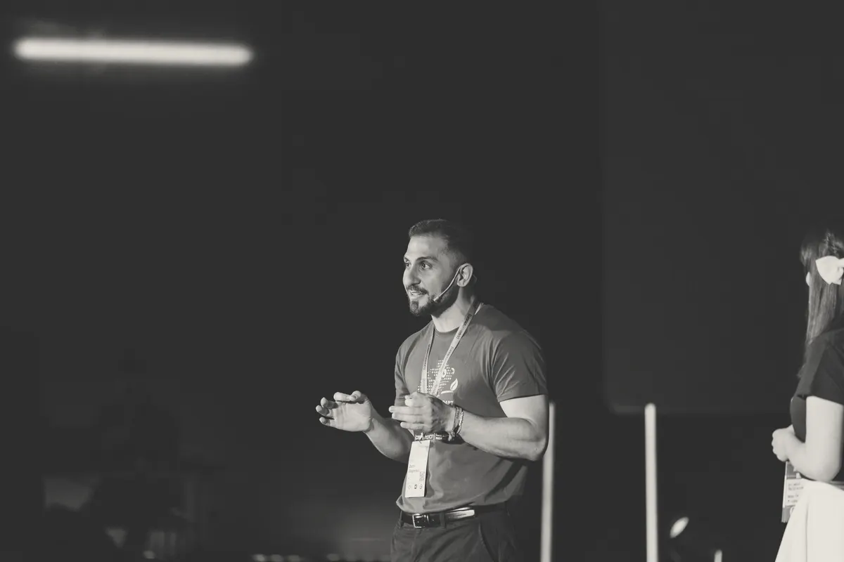 Mid-sentence on stage in a headset mic, hands out, explaining something.